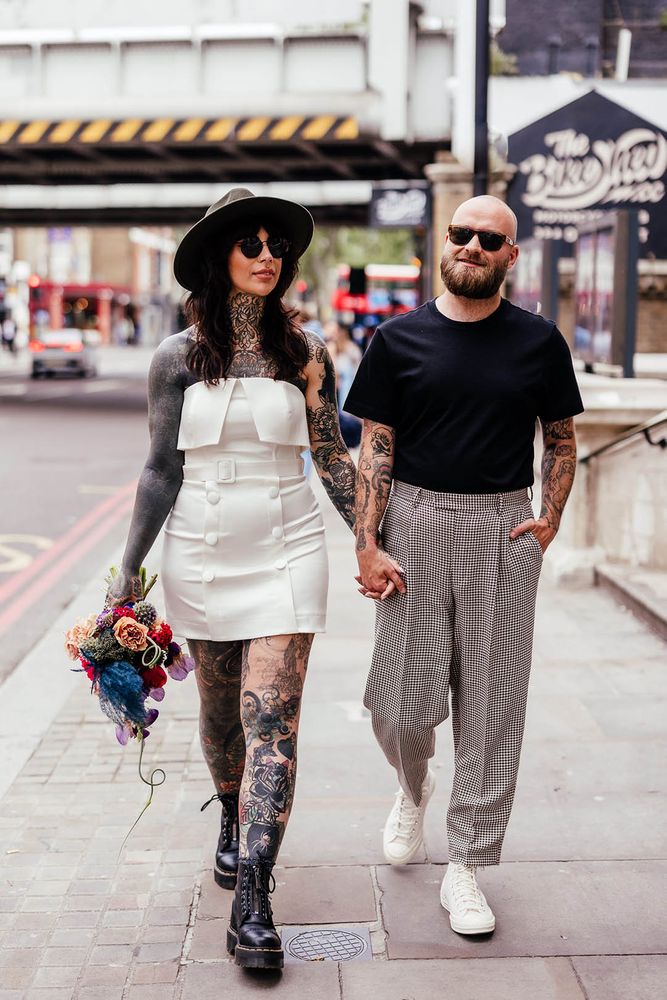 Alternative bride with tattoos in a strapless short wedding dress with button and belt detailing to the waist and front