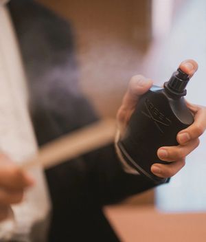 Groom spraying black Creed fragrance bottle on wedding day - Best Groom Fragrances For Your Wedding Day