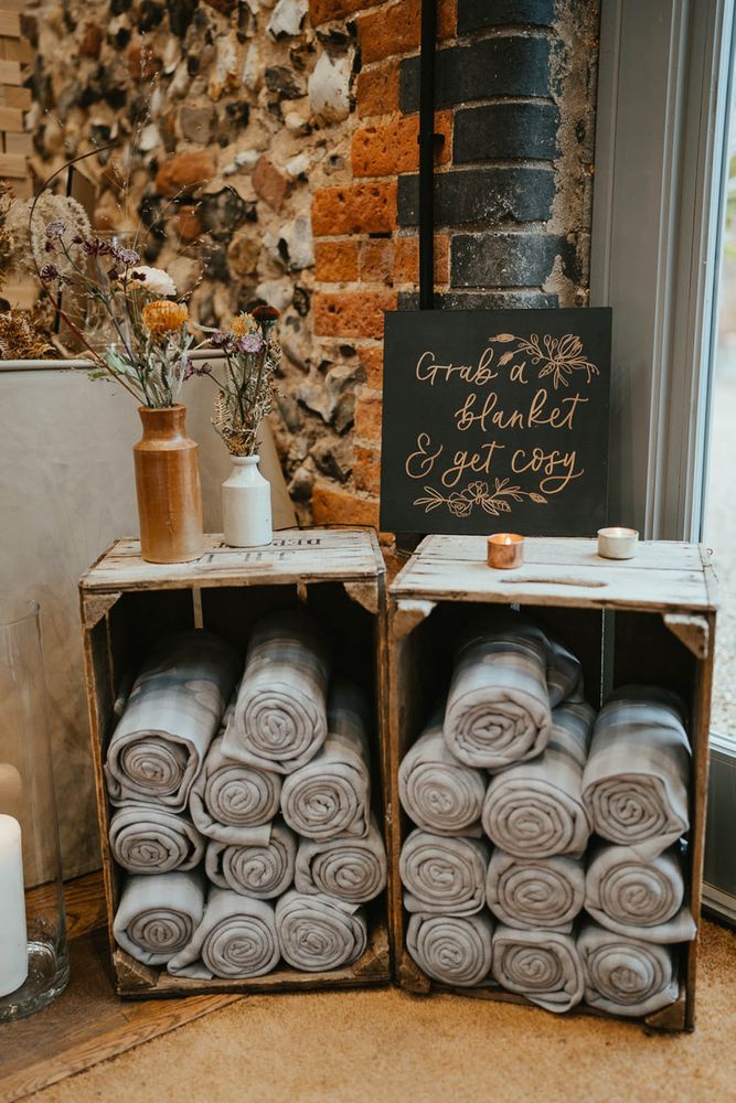 Wooden crates full of rolled up blankets for wedding guests to use as favours and get cosy