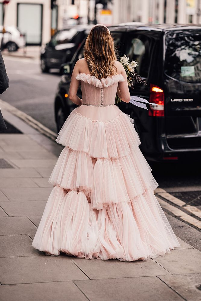 Bride wears blue pink wedding dress with fitted bodice complete with sheer fabric to the top and ruffled skirt 