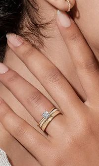 Close-up of a bride’s hand wearing stacked gold wedding rings and a diamond engagement ring - Wedding Rings & Bridal Jewellery