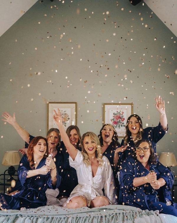 Bridesmaids in satin navy robes and pyjamas popping gold confetti canon as they get ready together