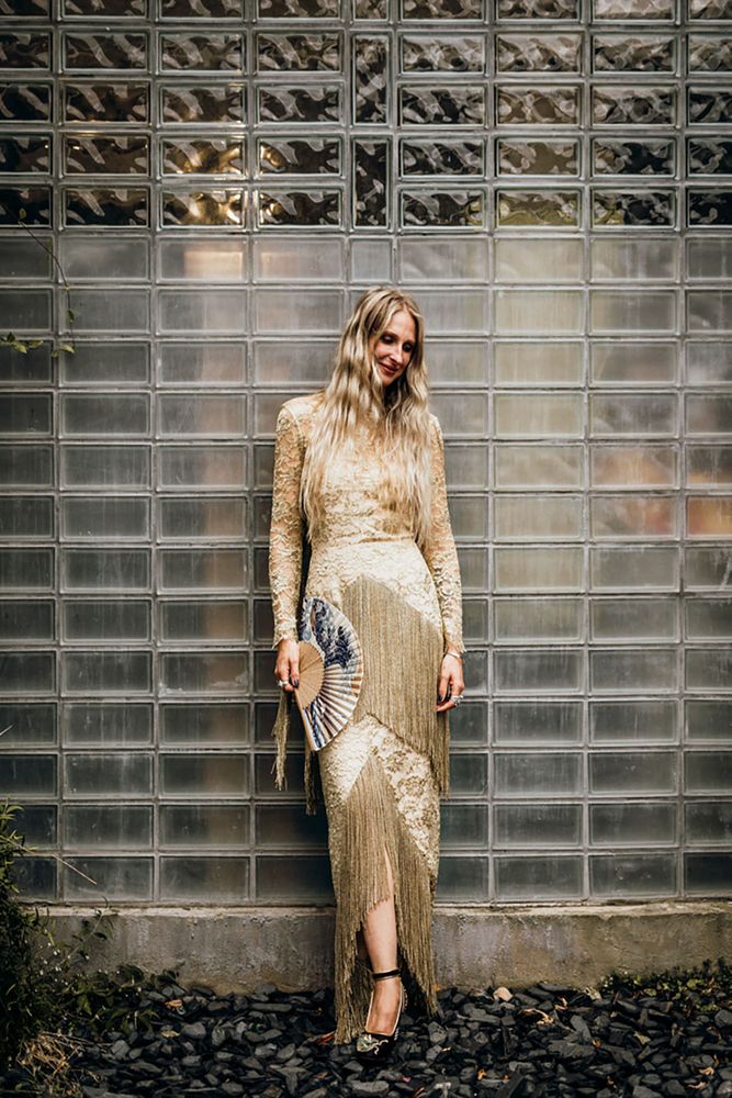 Bride wears her long blonde hair to the front in waves and gold wedding dress complete with tassels to the sleeves and front of dress