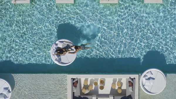 Couple enjoying a romantic moment at Once in Mykonos infinity pool – bride relaxing on a luxury white sunbed in pool while groom swims in crystal-clear water - Once In Mykonos Honeymoon Hotel Review