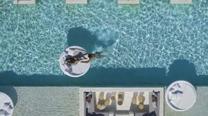 Couple enjoying a romantic moment at Once in Mykonos infinity pool – bride relaxing on a luxury white sunbed in pool while groom swims in crystal-clear water - Once In Mykonos Honeymoon Hotel Review