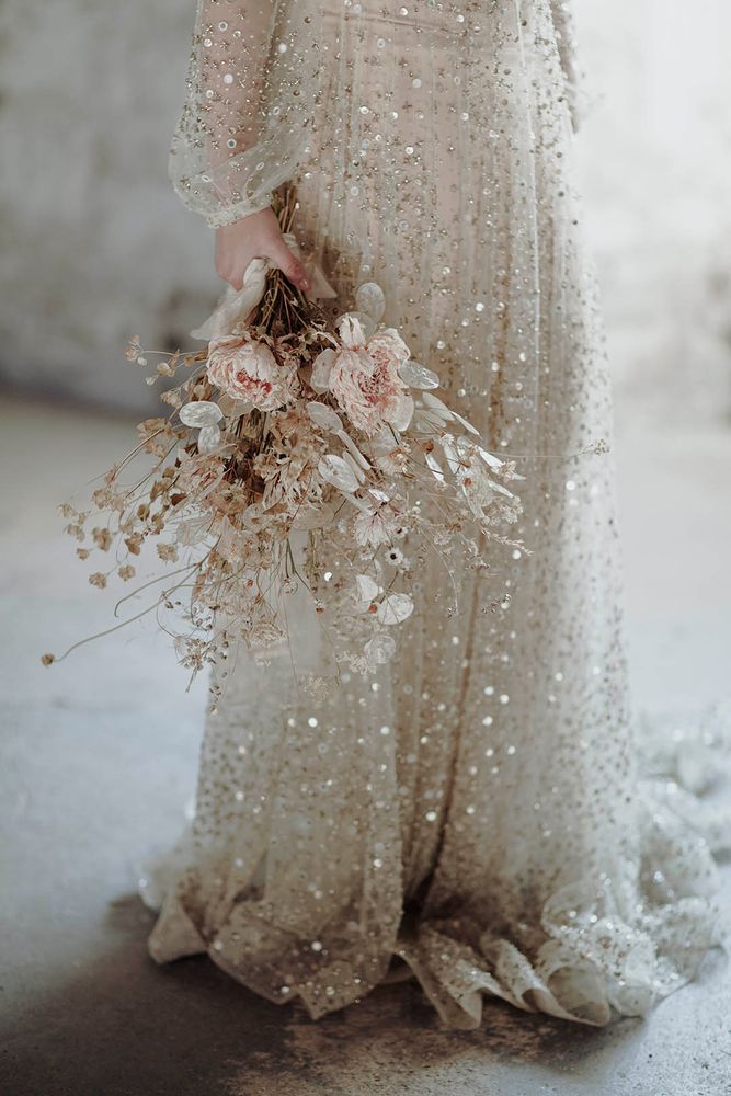 Bride wears sequin embellished wedding dress for alternative bridal outfit whilst carrying dried floral bouquet
