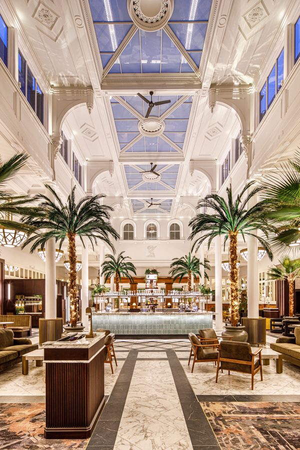 Palm Court bar inside The Municipal Hotel Liverpool, with marble floors, tall palm trees, and a central cocktail bar beneath a glass atrium - Best Hotel For Hen Party In Liverpool