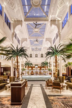 Palm Court bar inside The Municipal Hotel Liverpool, with marble floors, tall palm trees, and a central cocktail bar beneath a glass atrium - Best Hotel For Hen Party In Liverpool