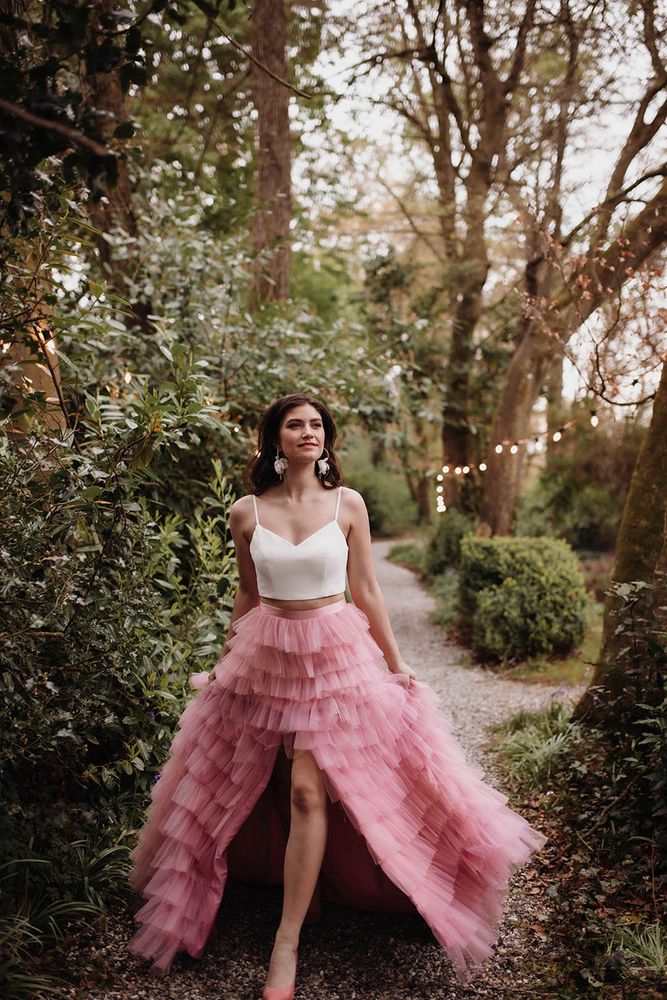 Bride wears white sweetheart neckline strappy crop top with ruffled pink skirt with high-low styling and silk waistband 
