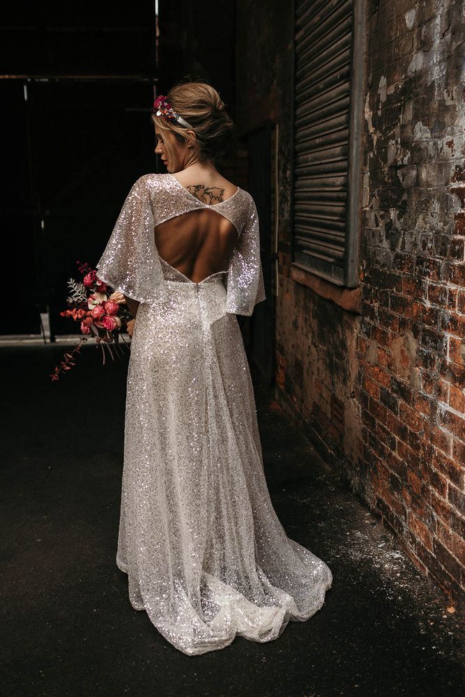 Bride wears open back batwing wedding dress with sparkling fabric whilst carrying colourful floral bouquet