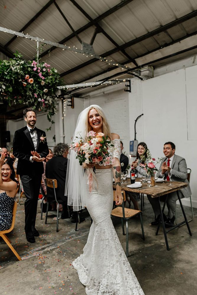 Bride wears lace fitted two-piece with off-the-shoulder styled top with 1/4 length sleeves 