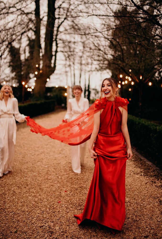 Bride wears high neck silky sleek red wedding dress with sheer cape complete with floral styled embellishment 